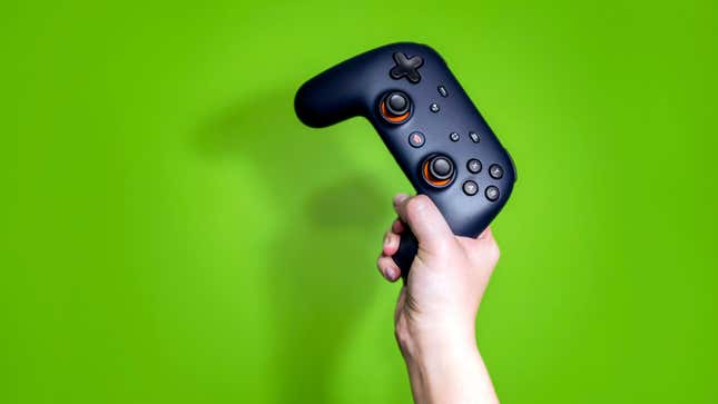 A hand holds a black Stadia controller up against a green background.