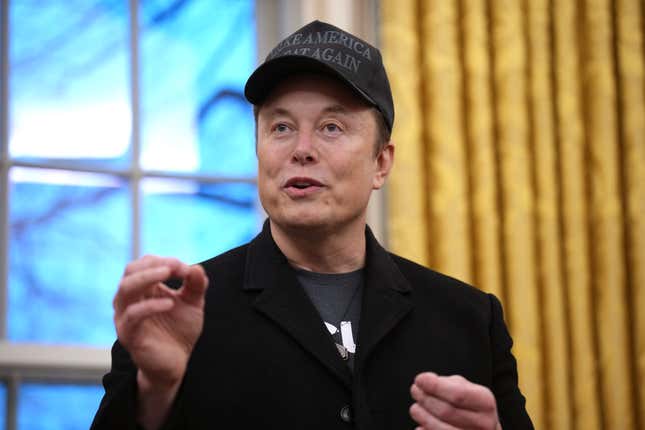 Elon Musk wearing a black make america great again hat speaking and gesturing with his hands