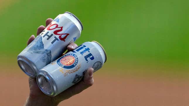 A hand holding up a can each of Coors Light and Miller Lite.