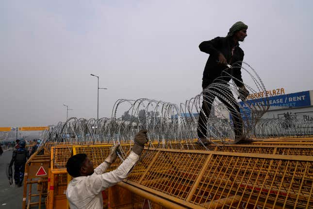 Workers put up barbed wire on top of barricades on a major highway at Singhu near New Delhi to stop thousands of protesting farmers from entering the capital, India, Tuesday, Feb.13, 2024. Farmers, who began their march from northern Haryana and Punjab states, are asking for a guaranteed minimum support price for all farm produce. (AP Photo/Manish Swarup)