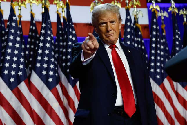 President-elect Donald Trump points while standing in front of a row of American flags