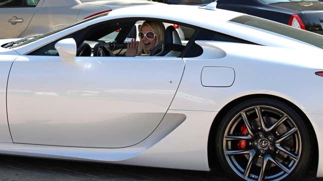 A photo of Paris Hilton wearing white sunglasses waving at the camera from inside her white Lexus LFA