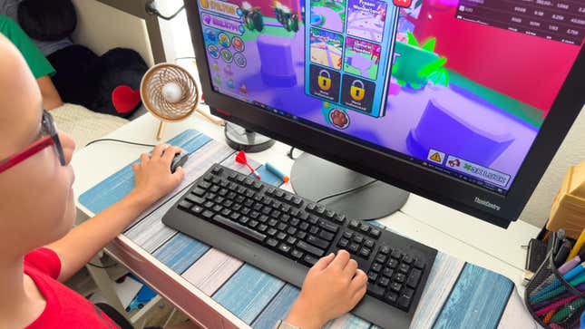 Boy playing a Roblox online multiplayer video game on a desktop in his room. Left handed user.