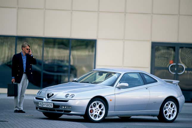 Front 3/4 view of a silver Alfa Romeo GTV with a businessman standing next to it