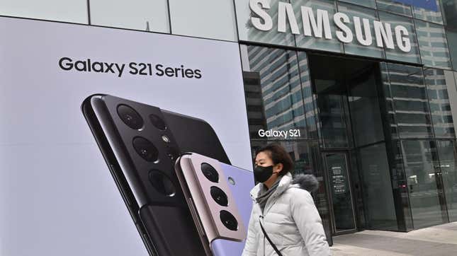 A woman walks by in front of a Samsung store and an advertisement for the Samsung Galaxy S21.