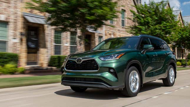 A dark green Toyota Highlander driving past some brick homes