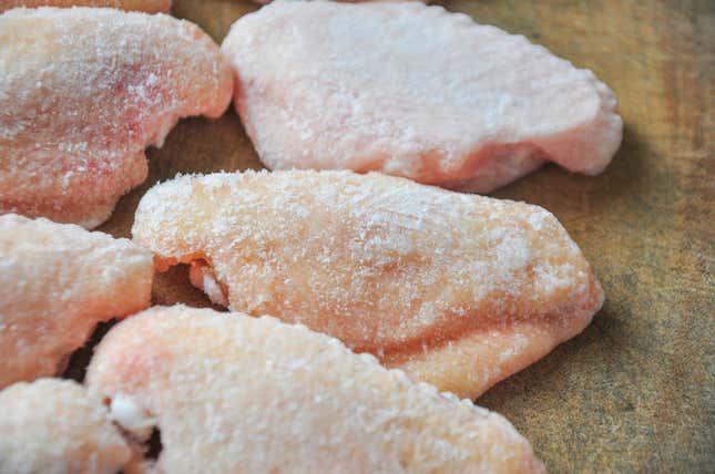 Six raw chicken wings on a greenish stoneware plate.