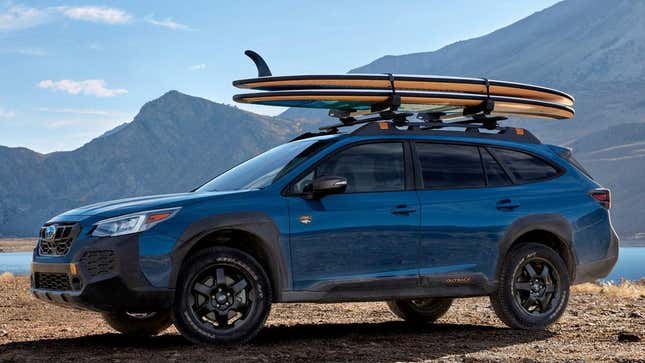 A Subaru Outback Wilderness parked by a scenic mountain lake with two surfboards on the roof rack