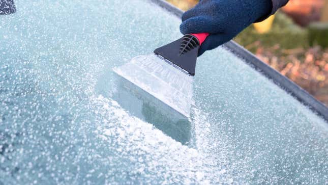 Mano con guante azul rascando hielo de la ventana de automóvil. El raspador de hielo es una extensión del brazo.