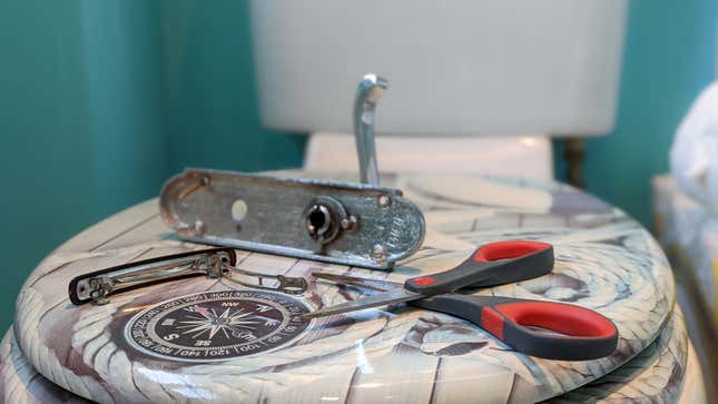 A photograph of a door handle, hair clip, and pair of scissors, beautifully arranged on a toilet seat.