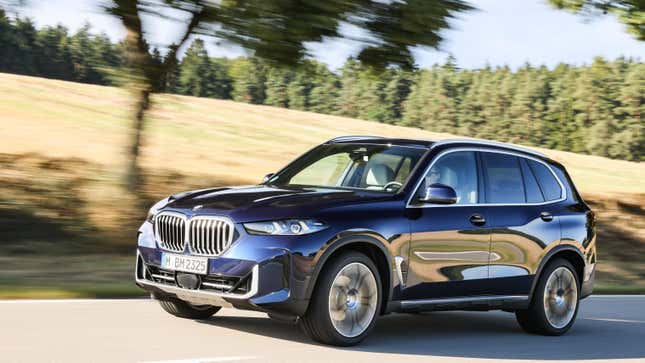 Un X5 bleu roulant devant un champ et une forêt