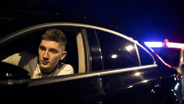 One young man looking at his rear mirror, pulled over by police, police car in the background