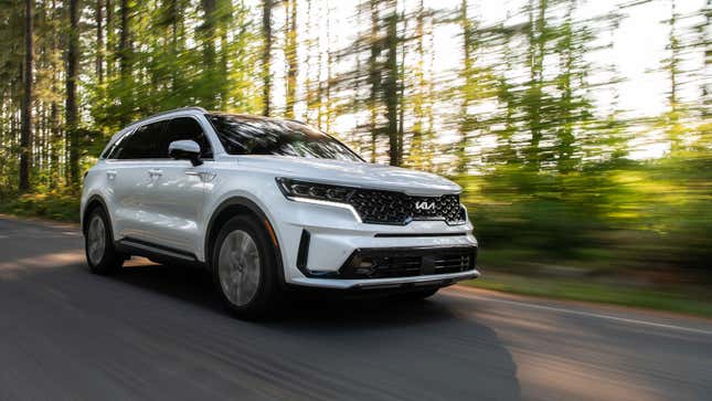 A photo of a white Kia Sorento SUV driving along a tree-lined road. 