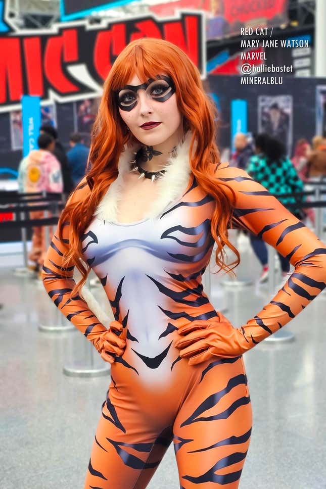 A cosplayer dressed as the Red Cat version of Mary Jane Watson stands with her hands on her hips.