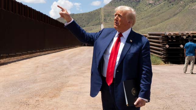 A photo of Donald Trump pointing at a wall. 