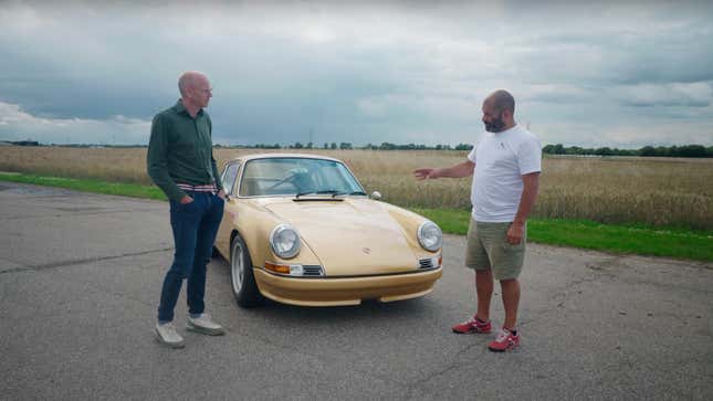 Two men, both bald, stand in front of a gold classic Porsche 911