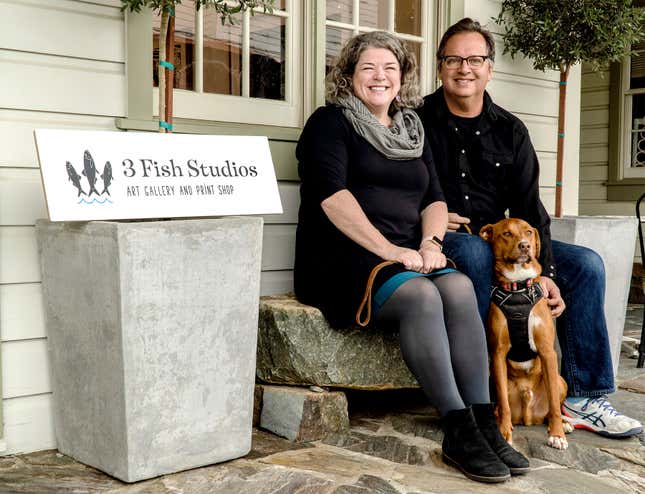 Husband and wife artist team Annie Galvin, left, and Eric Rewitzer pose with their dog Woody in front of their new 3 Fish Studios art gallery in Amador City, Calif., in 2023. Galvin and Rewitzer moved out of San Francisco to live closer to nature after their sabbatical in France and Ireland. (Eric Rewitzer via AP)