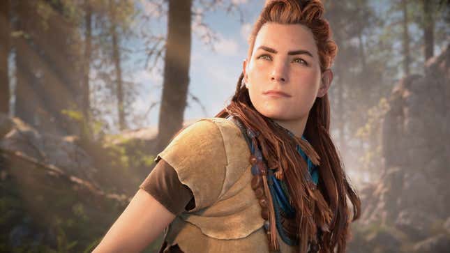 Aloy stands looking into the distance, in front of a woodland scene.