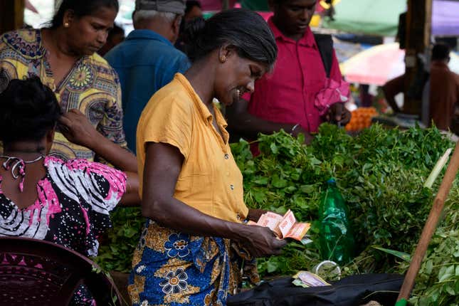 FILE- A vendor counts currency notes as she sells vegetables at a market place in Colombo, Sri Lanka, June. 1, 2023. Sri Lanka has reached an agreement with the Exim Bank of China on key terms and principles for restructuring its debt, a key step toward unlocking a second instalment of a $2.9 billion package from International Monetary Fund aimed at rescuing the island nation from a dire economic crisis. (AP Photo/Eranga Jayawardena, File)