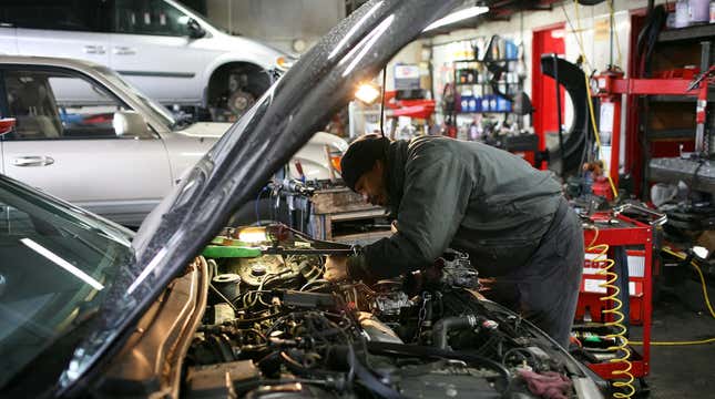 A mechanic is bent over under the hood of a car.