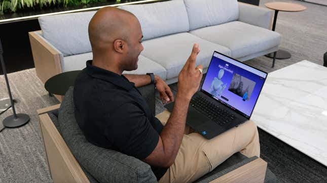 a view behind a man sitting in a chair holding his fingers up using an application on his laptop