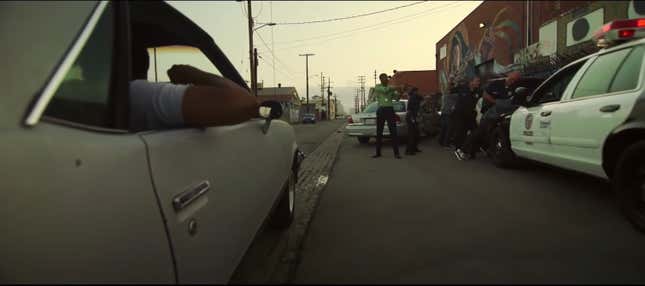 A young man hangs out of the window of a car as it drives past LAPD arresting other people