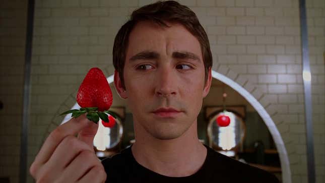 Lee Pace as Ned in Pushing Daisies holds a beautifully ripe strawberry in his fingers.
