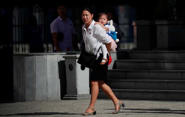 A woman carries her daughter as she waits to cross a street.
