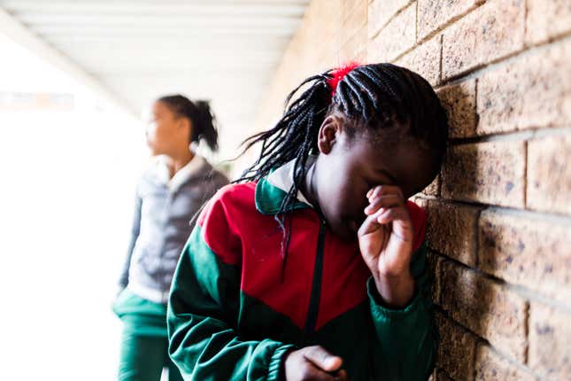 A stock photo of a school girl stands leaning against a wall crying, she is being bullied by other girls at her school. 