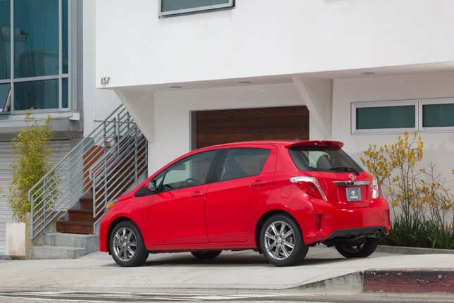 A red 2014 Toyota Yaris is parked in front of a modern home.