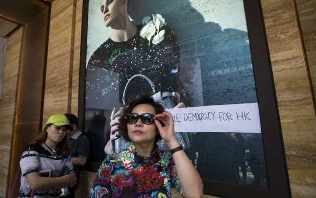 Chinese tourists walk past a slogan reading "True Democracy for HK" outside a luxury shop along a main street at Hong Kong's shopping district Tsim Sha Tsui October 1, 2014.Thousands of pro-democracy protesters thronged the streets of Hong Kong on Wednesday, ratcheting up pressure on the pro-Beijing government that has called the action illegal, with both sides marking uneasy National Day celebrations.