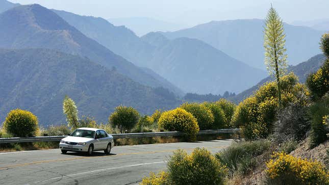 A photo of a small sedan driving up a mountain road. 