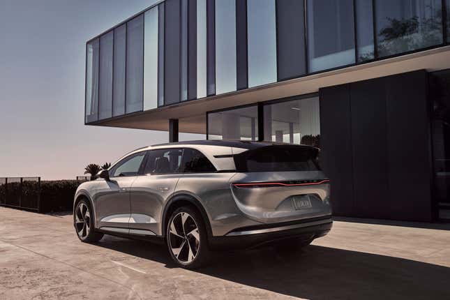 Lucid Gravity electric SUV in silver parked near a glass building.