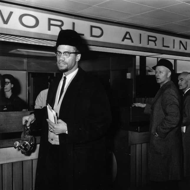 Malcolm X (1925 - 1965) arrives at London Airport carrying a portable cinecamera.