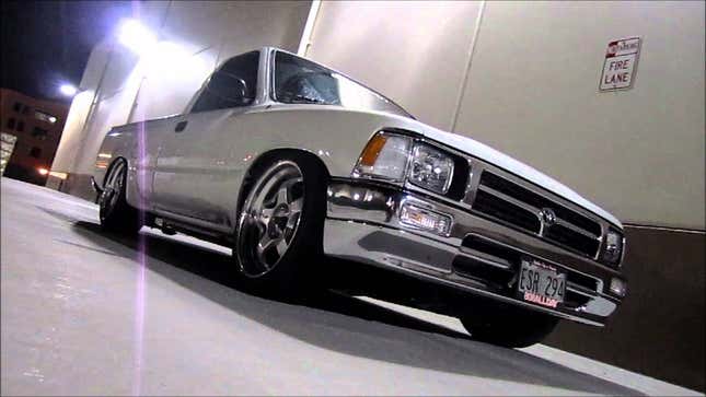 A stanced white Toyota pickup parked in front of a wall