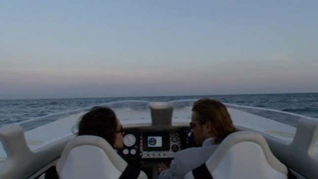 Gong Li and Colin Farrell look at each other while on a speedboat during sunset. 