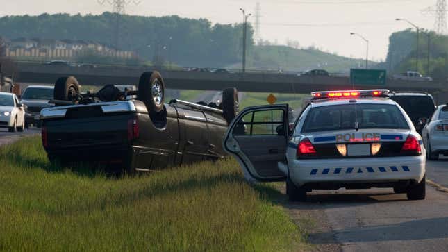 A police car responding to a truck upside down on a highway median