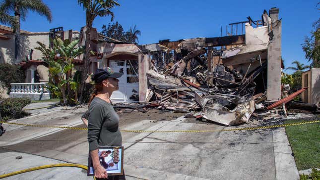 Lynn Morey stands in front of her burned home holding a portrait of her and her husband, Keith Morey, recovered by a firefighter after homes were destroyed by the Coastal Fire in Laguna Niguel, California, May 12, 2022.