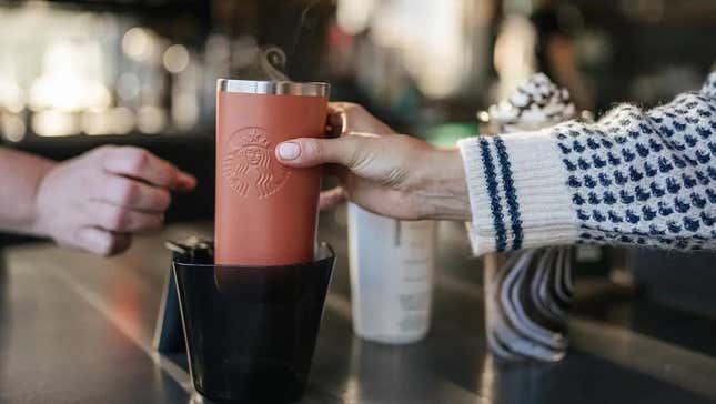 O barista do Starbucks entrega a um cliente sua bebida em uma garrafa térmica reutilizável.