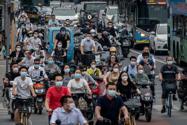 Commuters, many wearing protective masks, are seen in heavy traffic during rush hour at an intersection