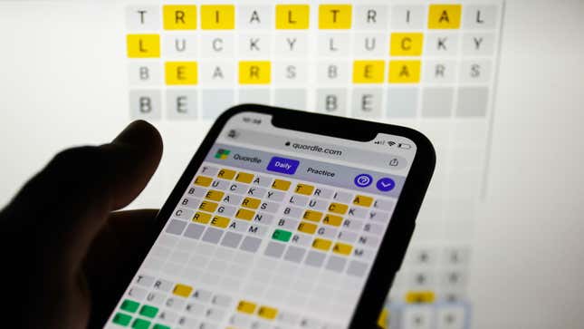 A person holding a phone playing Quordle, in front of a screen also playing Quordle, for some odd reason.