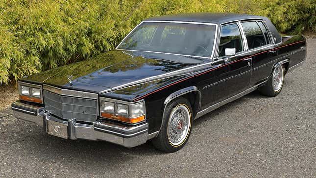 a black cadillac fleetwood parked in front of a bush