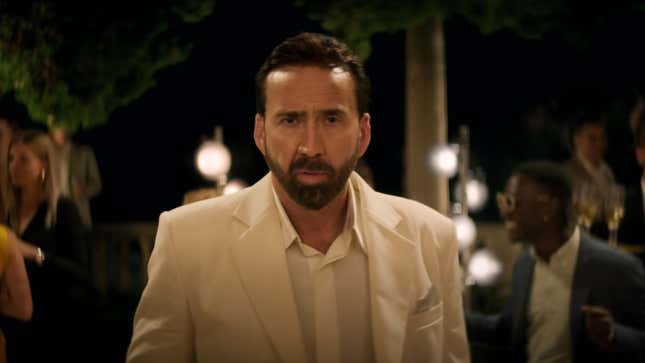 A perplexed Nic Cage stands in a white suit at a fancy outdoor party at night.
