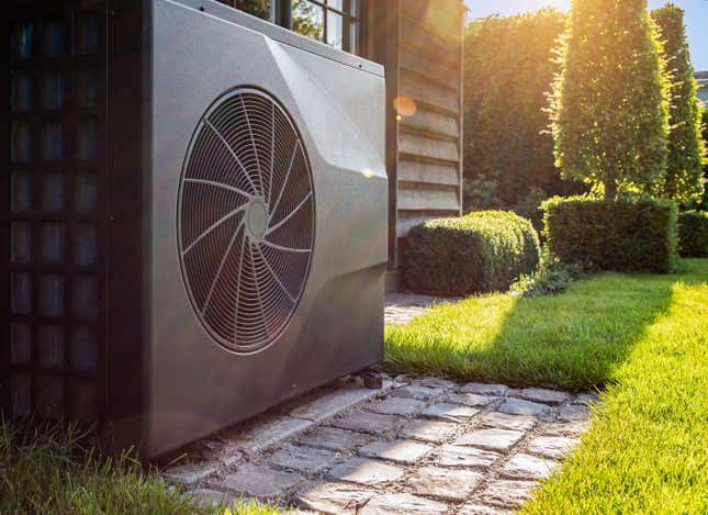 Close-up of black full inverter heat pump outside in the garden, near wooden pool house on a sunny day