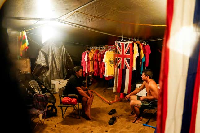 Blake Ramelb, left, talks with De Andre Makakoa, right, in Makakoa&#39;s tent at a housing protest on Kaanapali Beach Wednesday, Dec. 6, 2023, in Lahaina, Hawaii. A group of survivors is camping on the resort beach to protest and raise awareness for better long-term housing options for those displaced. Residents and survivors still dealing with the aftermath of the August wildfires in Lahaina have mixed feelings as tourists begin to return to the west side of Maui, staying in hotels still housing some displaced residents. (AP Photo/Lindsey Wasson)