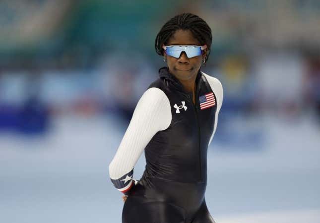 US speed skater Erin Jackson during training, wearing the US uniform and sunglasses, with her hands behind her back.