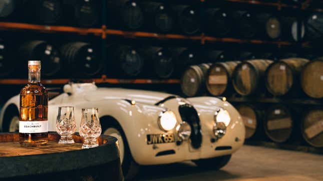 A photo of a bottle of Coachbuilt Whisky in front of an old car. 