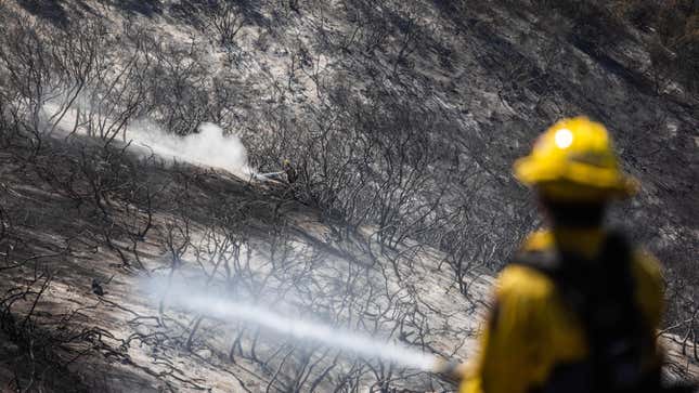 Firefighters fight hotspots in a burned canyon behind homes destroyed by the Coastal Fire in Laguna Niguel, California, May 12, 2022. 