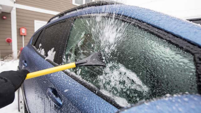 A photo of an ice scraper clearing a car window with shards of ice flying into the air. 