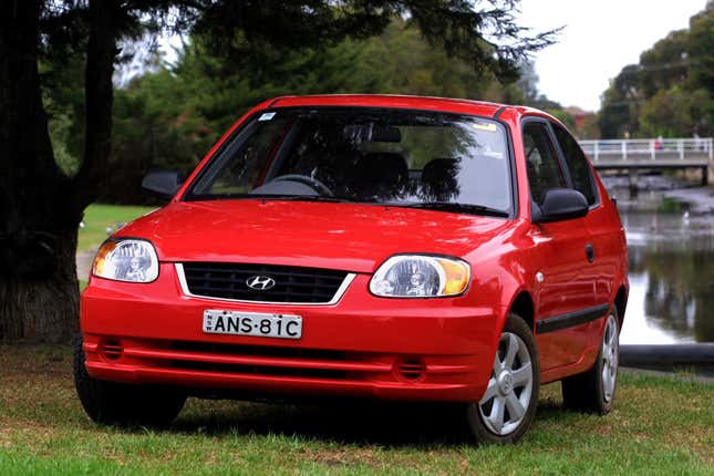 un Hyundai Accent rojo estacionado sobre el césped junto a un lago